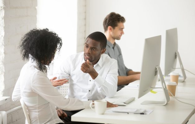 Serious african colleagues discussing project together at workplace, black coworkers talking solving business problem in multiracial office, afro american teammates having disagreement or conflict at work